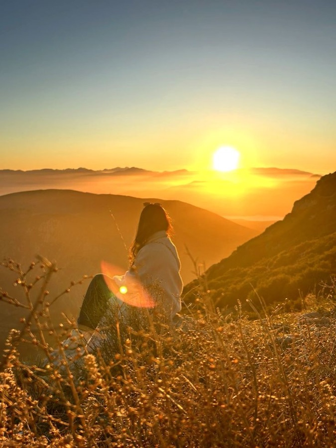 Mulher contemplando o pôr do sol na serra