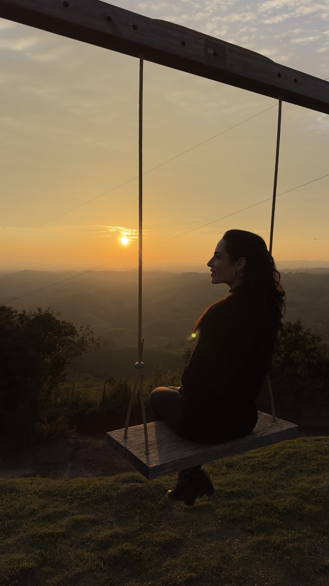 Mariah Ruibal, anfitriã do Entre Páginas, em um balanço diante do pôr do sol na serra